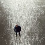 man wearing black jacket standing on frozen body of water during daytime