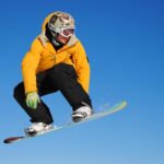 man in yellow jacket and blue pants riding on white snowboard